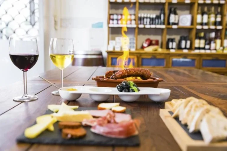 Portuguese petiscos tasting on a wooden table: red and white wine, flambéed chouriço, olives, cheese, cured meats and bread