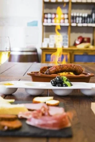 Portuguese petiscos tasting on a wooden table: red and white wine, flambéed chouriço, olives, cheese, cured meats and bread